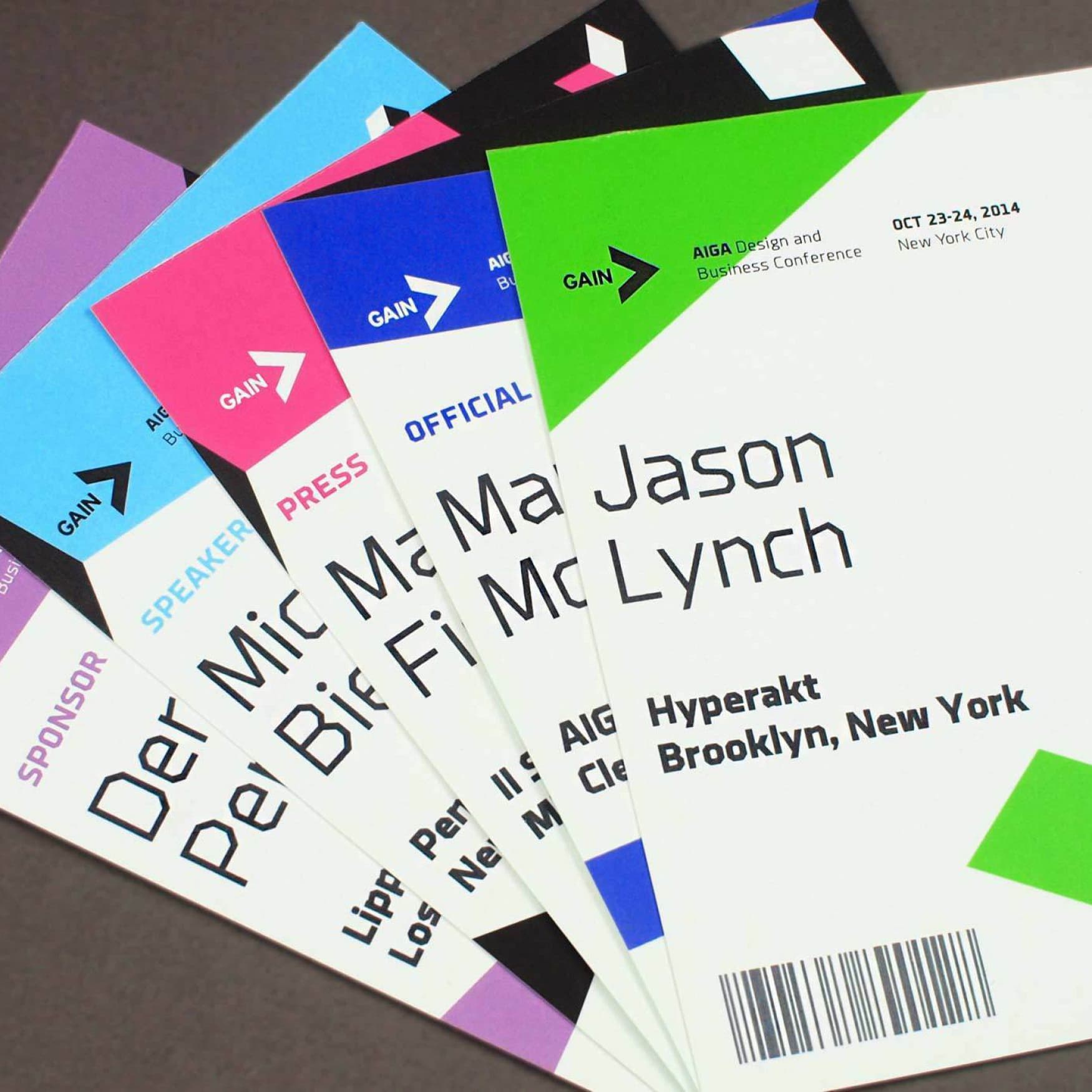Several colorful conference name badges arranged fanned out on a table. The badges display names and titles such as "Jason Lynch," along with designations like "SPONSOR" and "PRESS." The event is "GAIN AIGA Design and Business Conference" held on Oct 23-24, 2014.