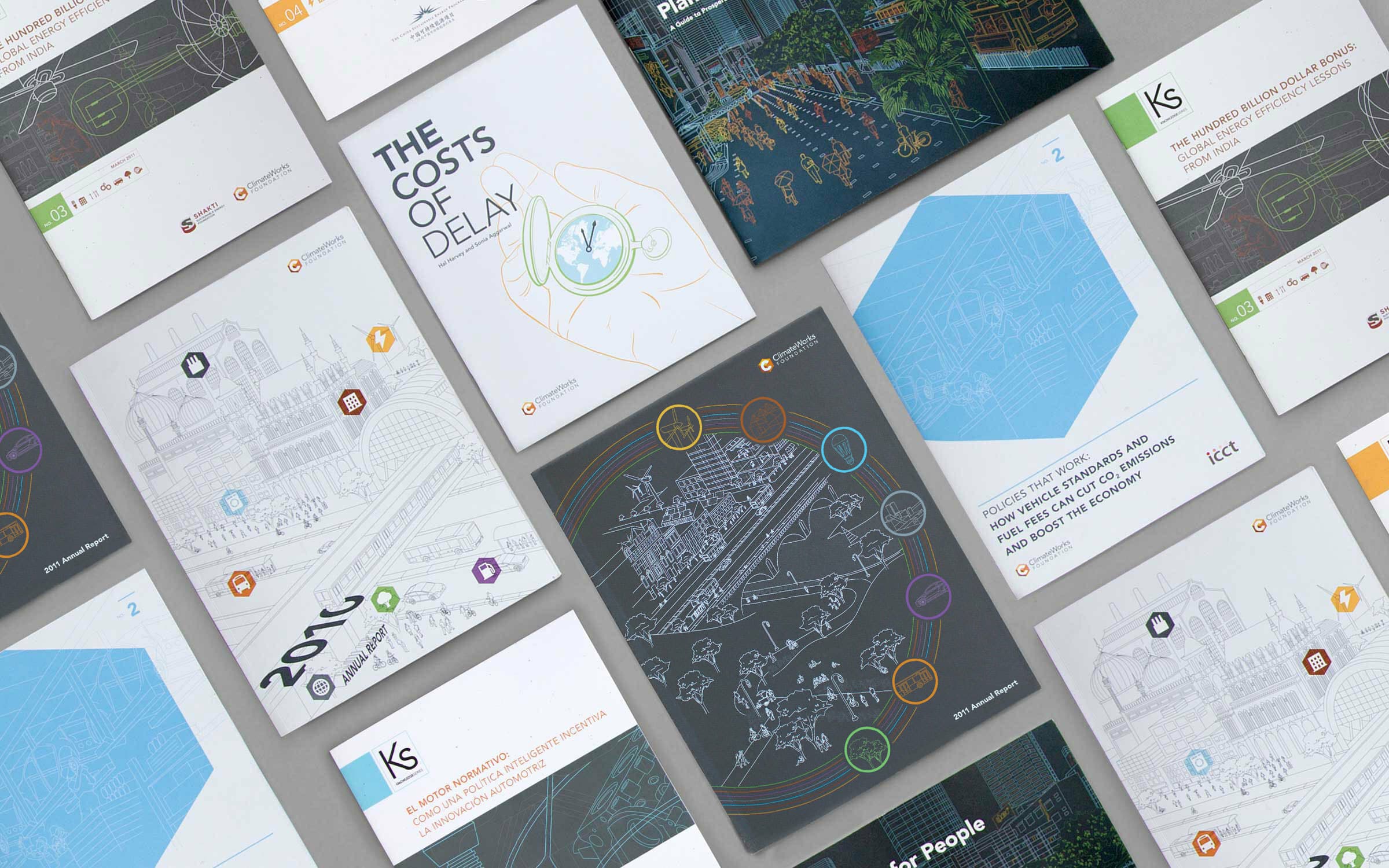 A top-down view shows an array of colorful and monochromatic books and reports spread out on a flat surface. The covers display various illustrations, diagrams, and text, focusing on topics like cost analysis, planning, and development.