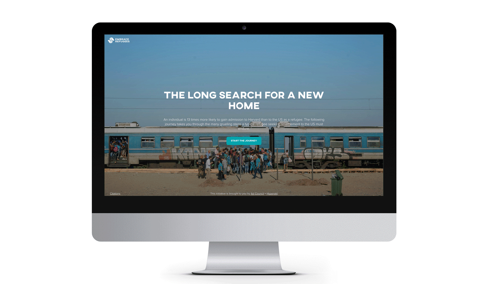 A computer monitor displaying a website with a header that reads "THE LONG SEARCH FOR A NEW HOME." The background shows a group of people standing near a train. Below the header is a button labeled "START THE JOURNEY." The website footer credits the International Rescue Committee.
