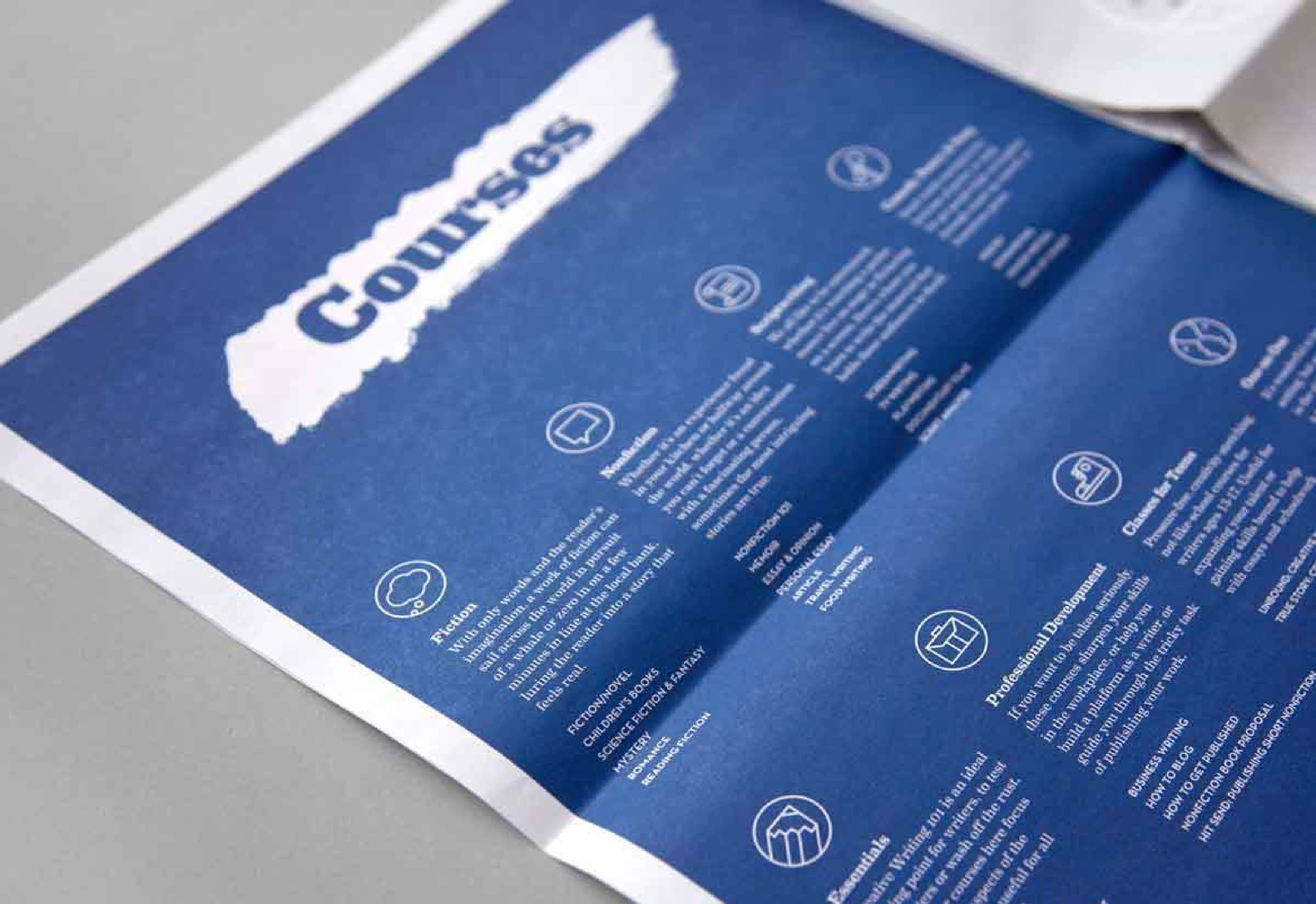 A blue pamphlet titled "Courses" lays flat on a surface. It features multiple sections, each with an icon and descriptive text under different course headings, providing detailed information about various educational offerings.