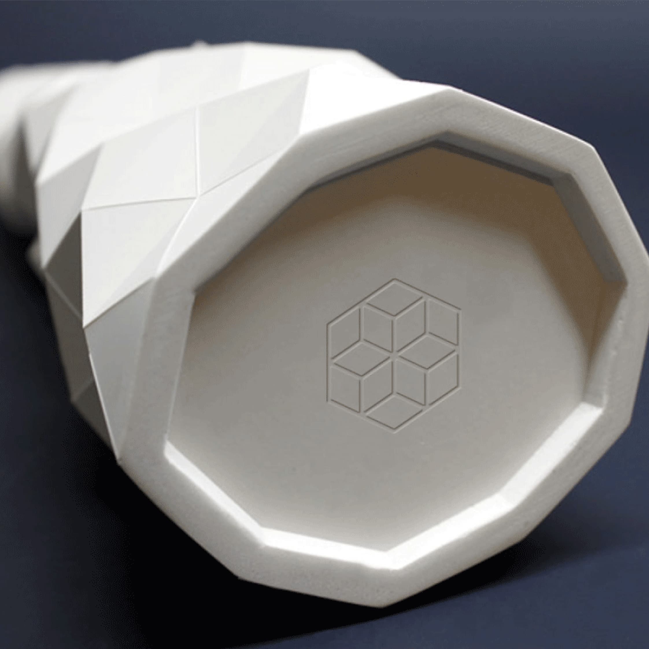 Geometric, faceted vase with a hexagonal base and an embossed cube pattern at the bottom, displayed against a dark background.