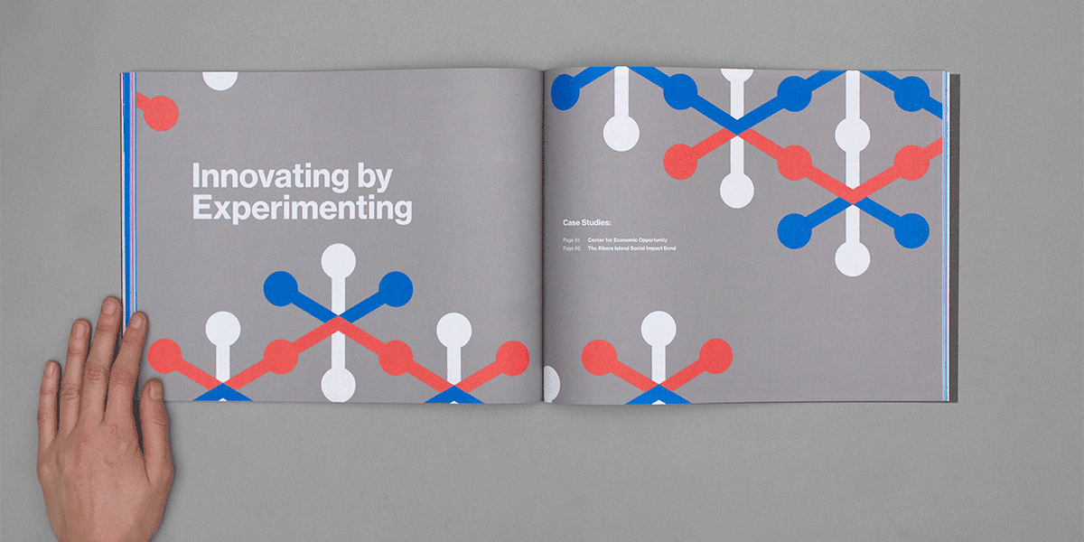 An open book on a gray surface, with the left page displaying the text "Innovating by Experimenting" and the right page showing "Case Studies" with colorful, abstract molecular patterns in blue, red, and white spread across both pages. A hand is holding the left edge of the book.