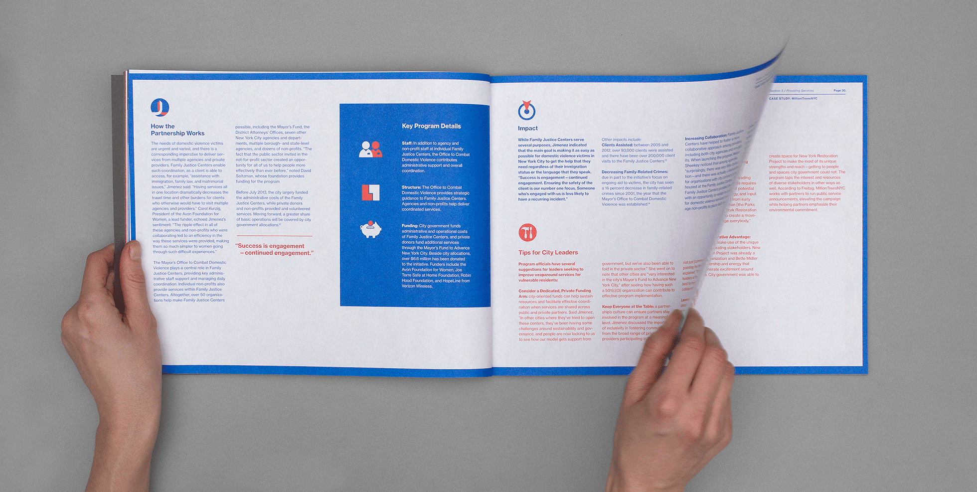 A person's hands holding open a booklet with a blue border and colorful text sections in red, blue, and black. Content includes program details, impacts, and tips for city leaders. The person is in the process of turning a page. Background is grey.