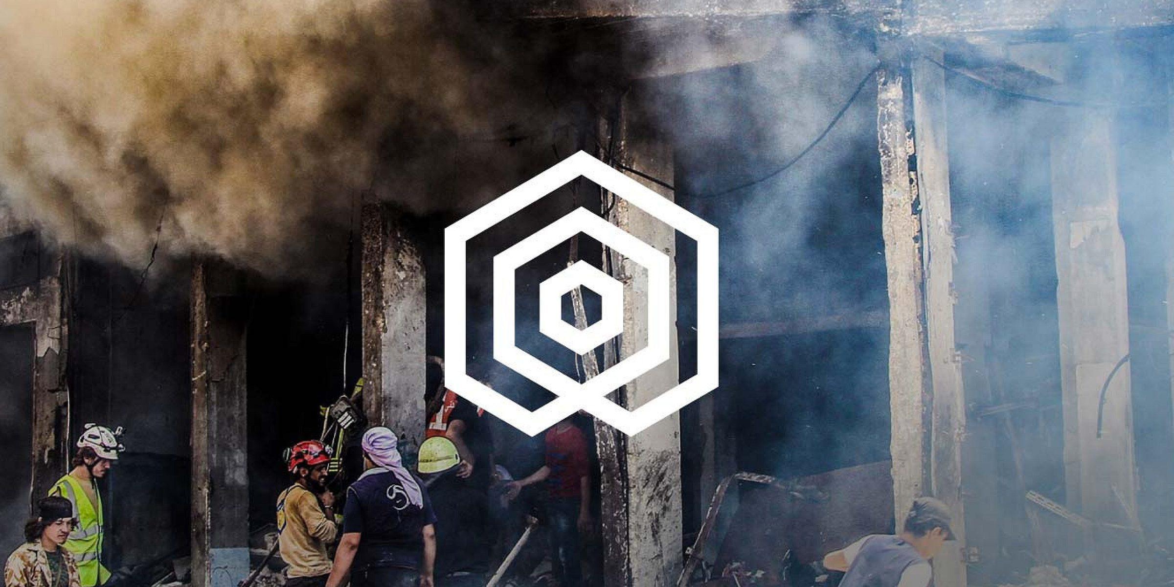 A group of people, some in safety gear, gather amidst debris and smoke in a damaged building. Thick smoke partially obscures the scene. At the center of the image, there is a superimposed geometric logo consisting of concentric hexagons.