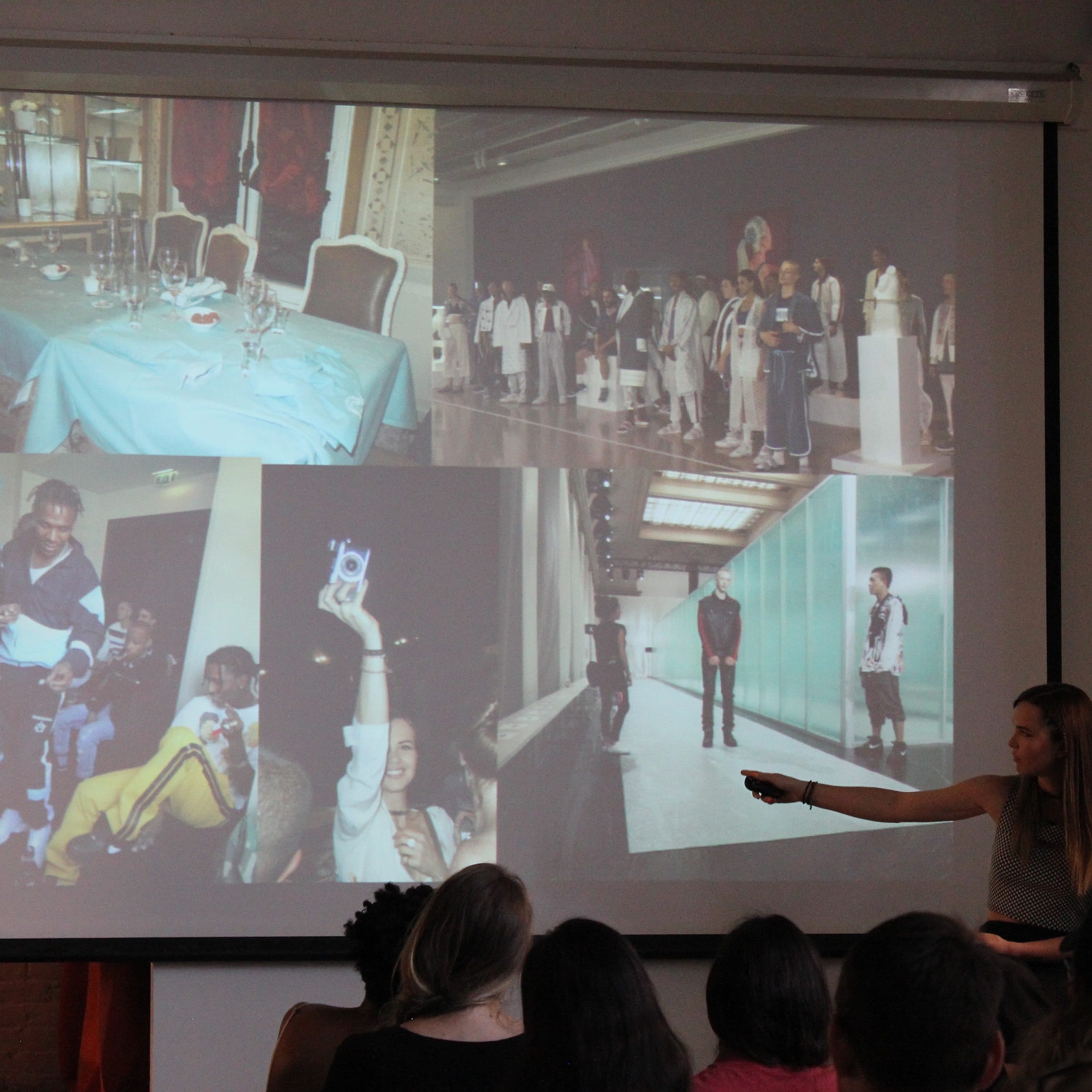 A woman stands and points at a presentation screen displaying various fashion images. The audience sits facing the screen, showing interest. The images include models on runways, people holding items, group pictures, and artistic settings.