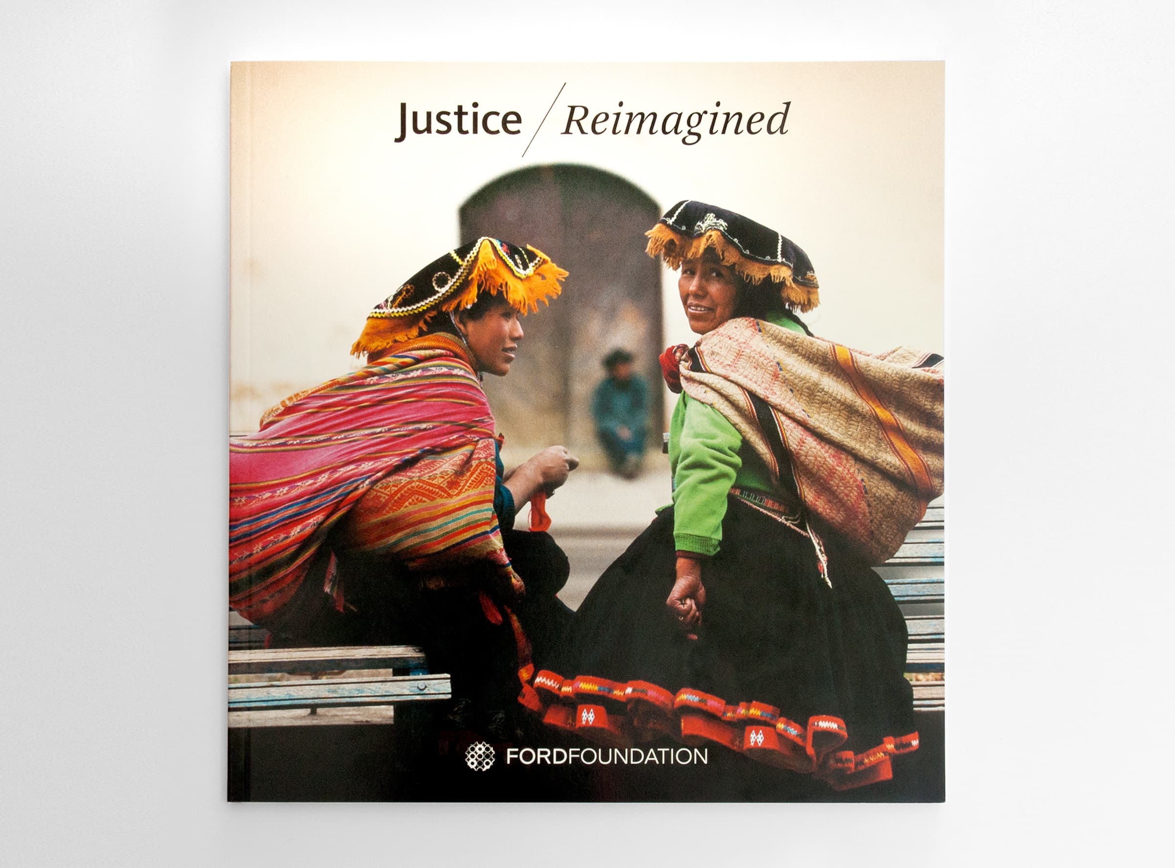 Cover of a book titled "Justice Reimagined" with two individuals in traditional costumes sitting and conversing. They wear vibrant, colorful textiles and ornate hats. The Ford Foundation logo is at the bottom of the cover.