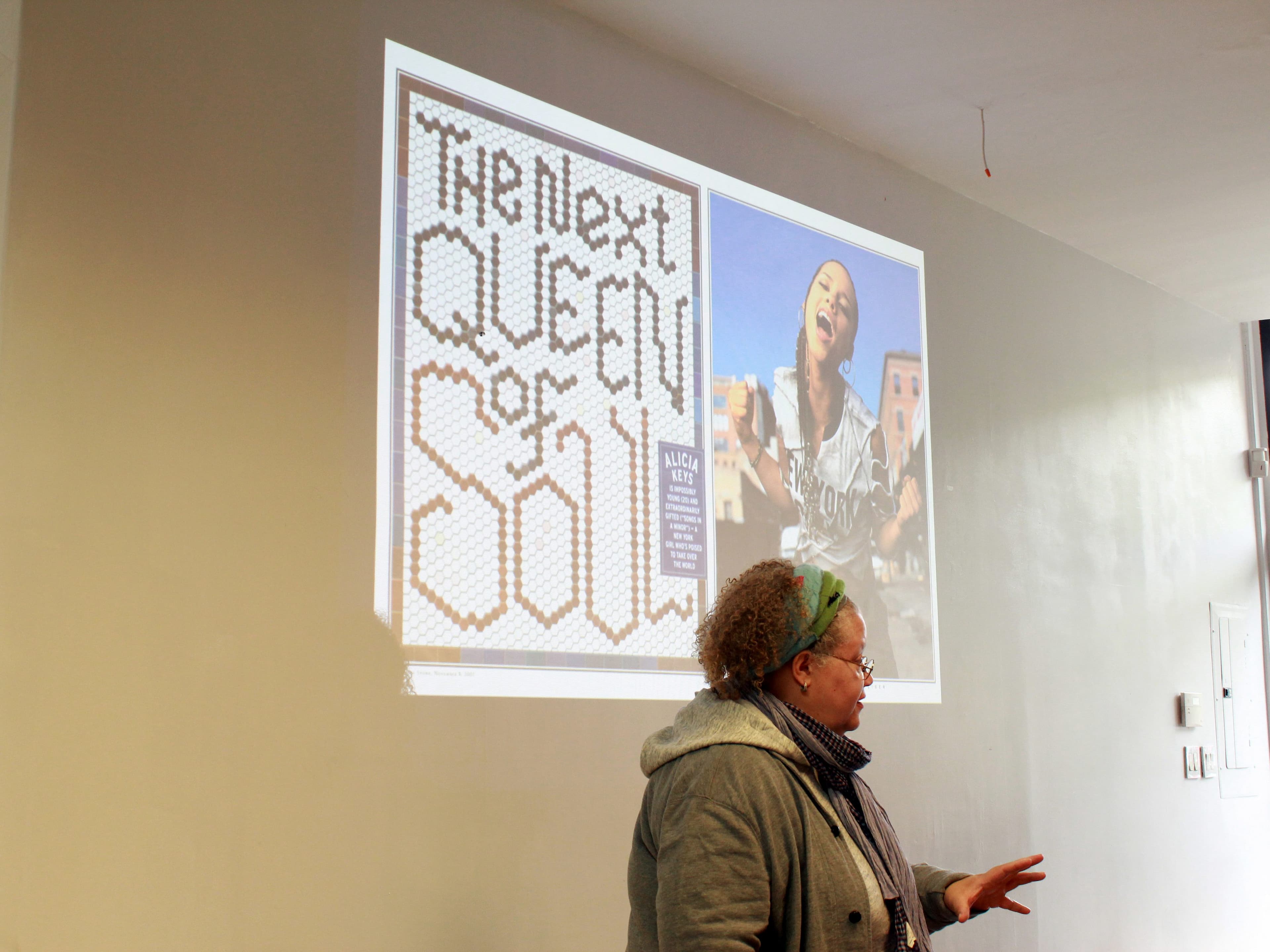 A person stands in front of a projected presentation in a bright room. The slide displays the text "The Next Queen of Soul" in a creative font, alongside an image of a woman singing passionately. The presenter is gesturing while speaking.