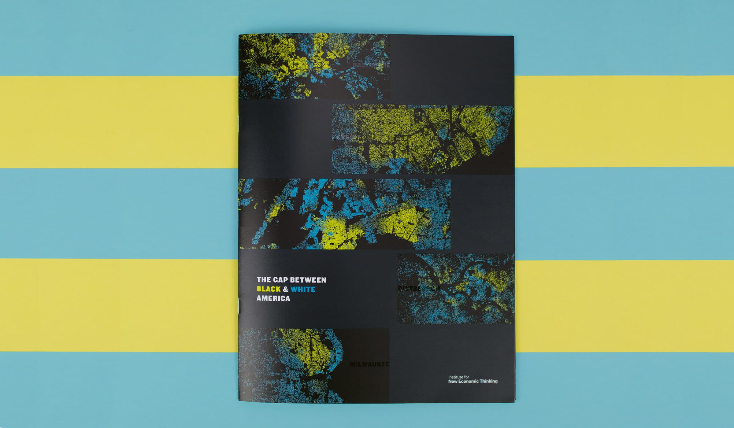 A brochure placed on a teal and yellow background displays a cover featuring a mosaic of abstract artworks in blue, yellow, and black. The title reads "The Gap Between Black & White America.