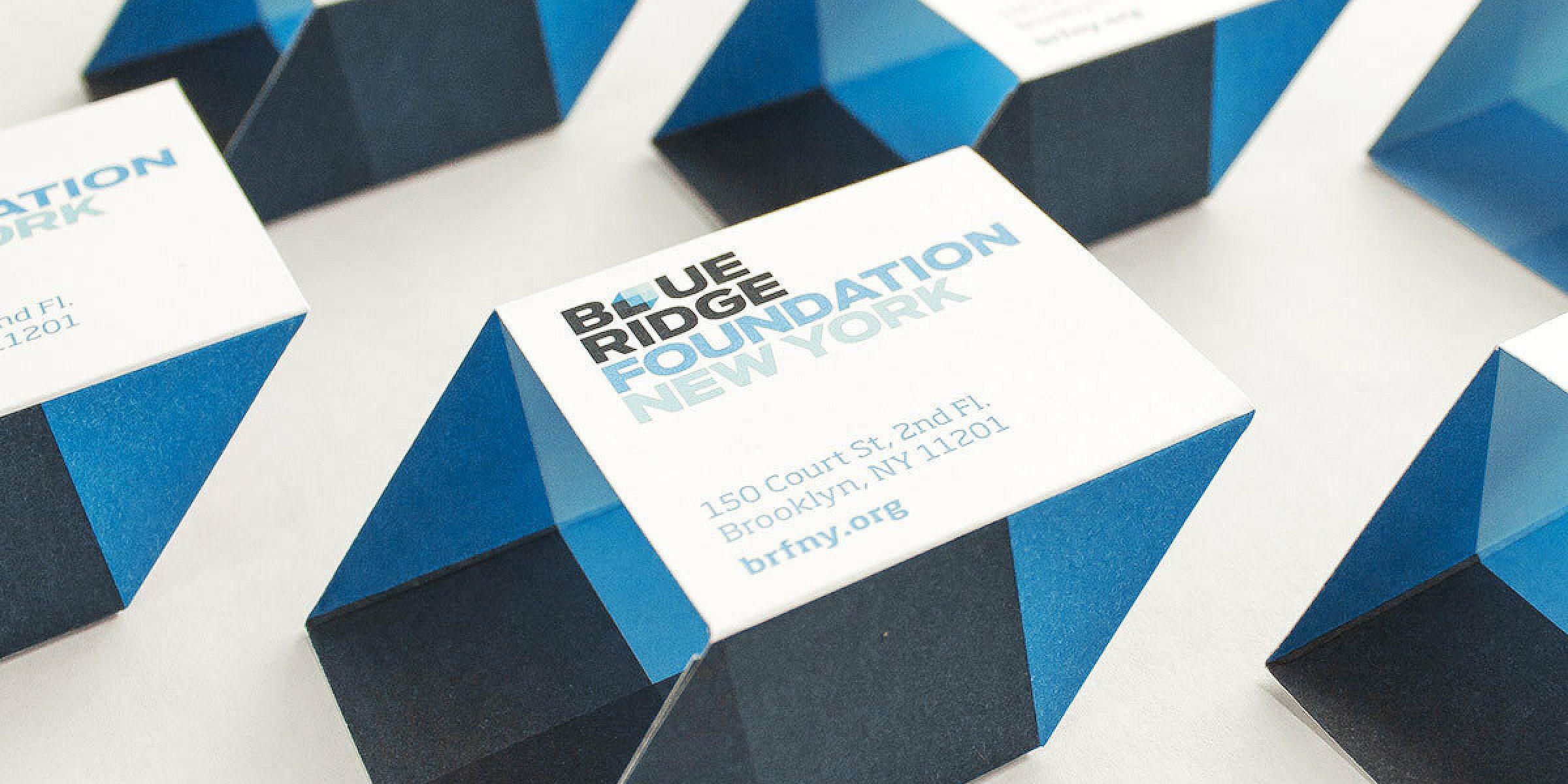 A set of uniquely shaped business cards for Blue Ridge Foundation New York are arranged on a white surface. The cards have a 3D geometric design with blue and dark blue sections. The text includes the organization's name, address, and website.