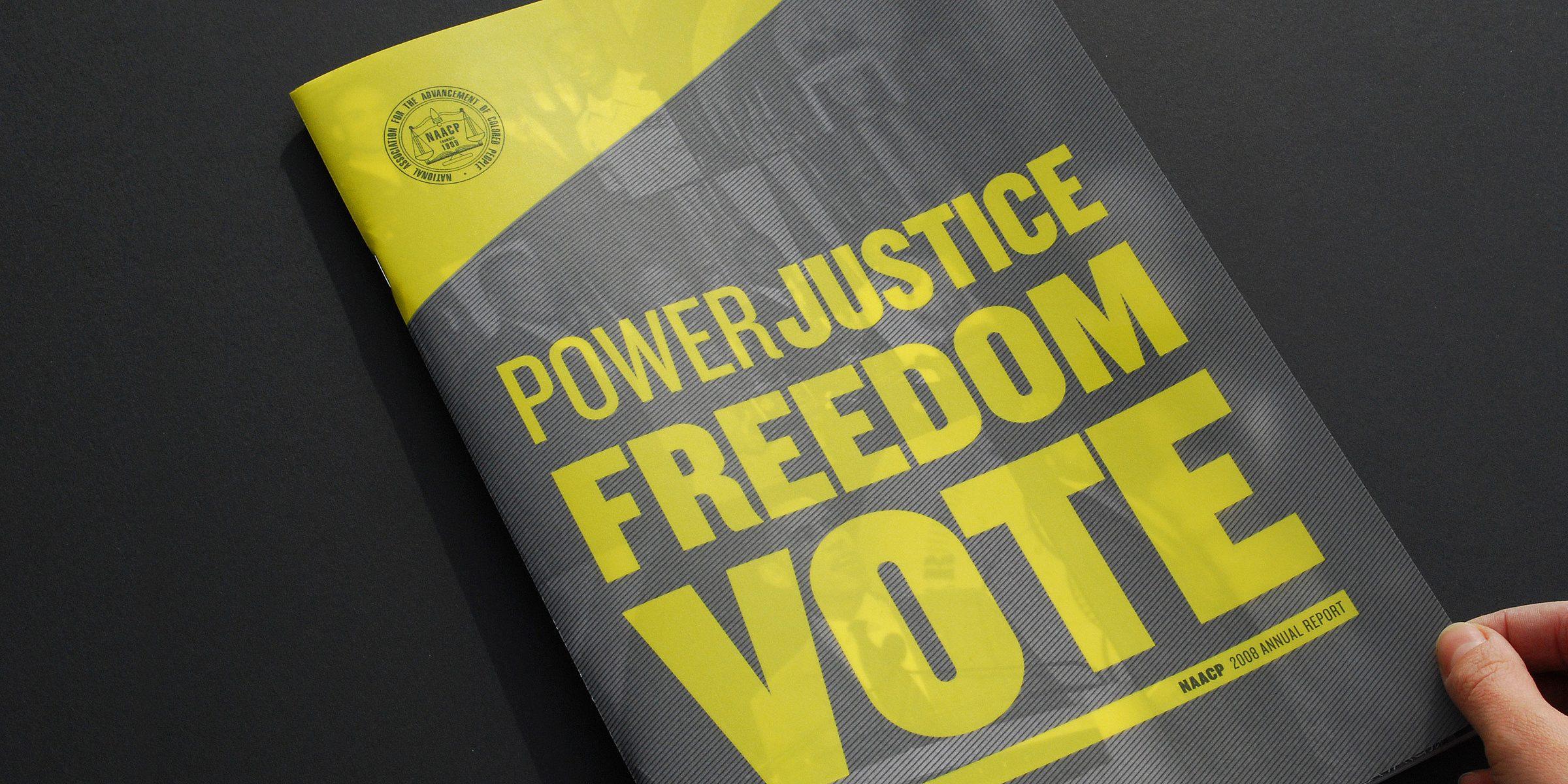 A hand holding a magazine with a black and yellow cover. The magazine features bold, large text in yellow and white that reads "POWER, JUSTICE, FREEDOM, VOTE" and "NAACP 2022 ANNUAL REPORT" in smaller print. The background includes a subtle image of people.