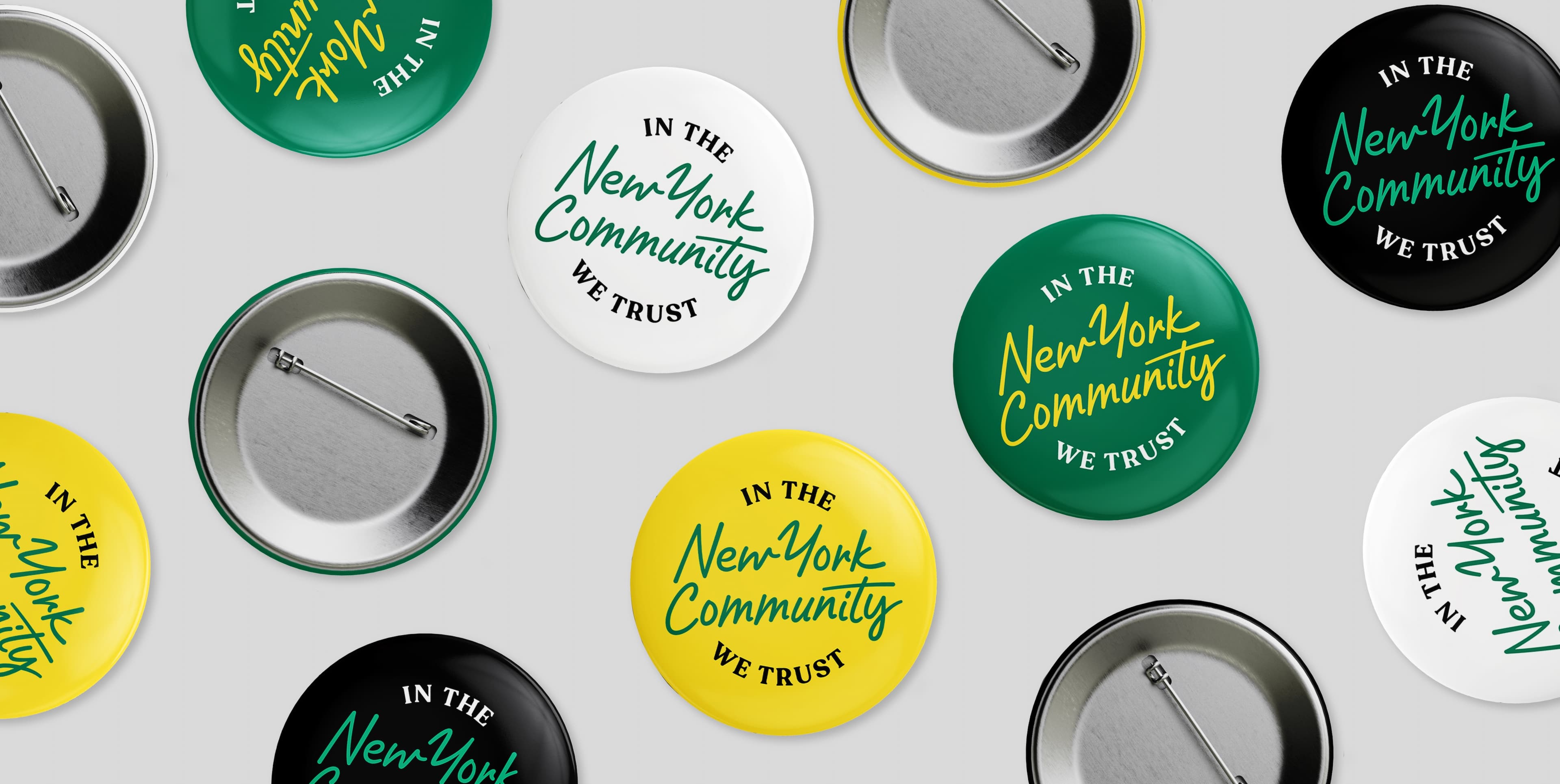 Several circular pins are spread out on a light gray surface. The pins feature texts in different colors and fonts, stating "IN THE New York Community WE TRUST." The pins come in various colors, including yellow, black, green, and white.