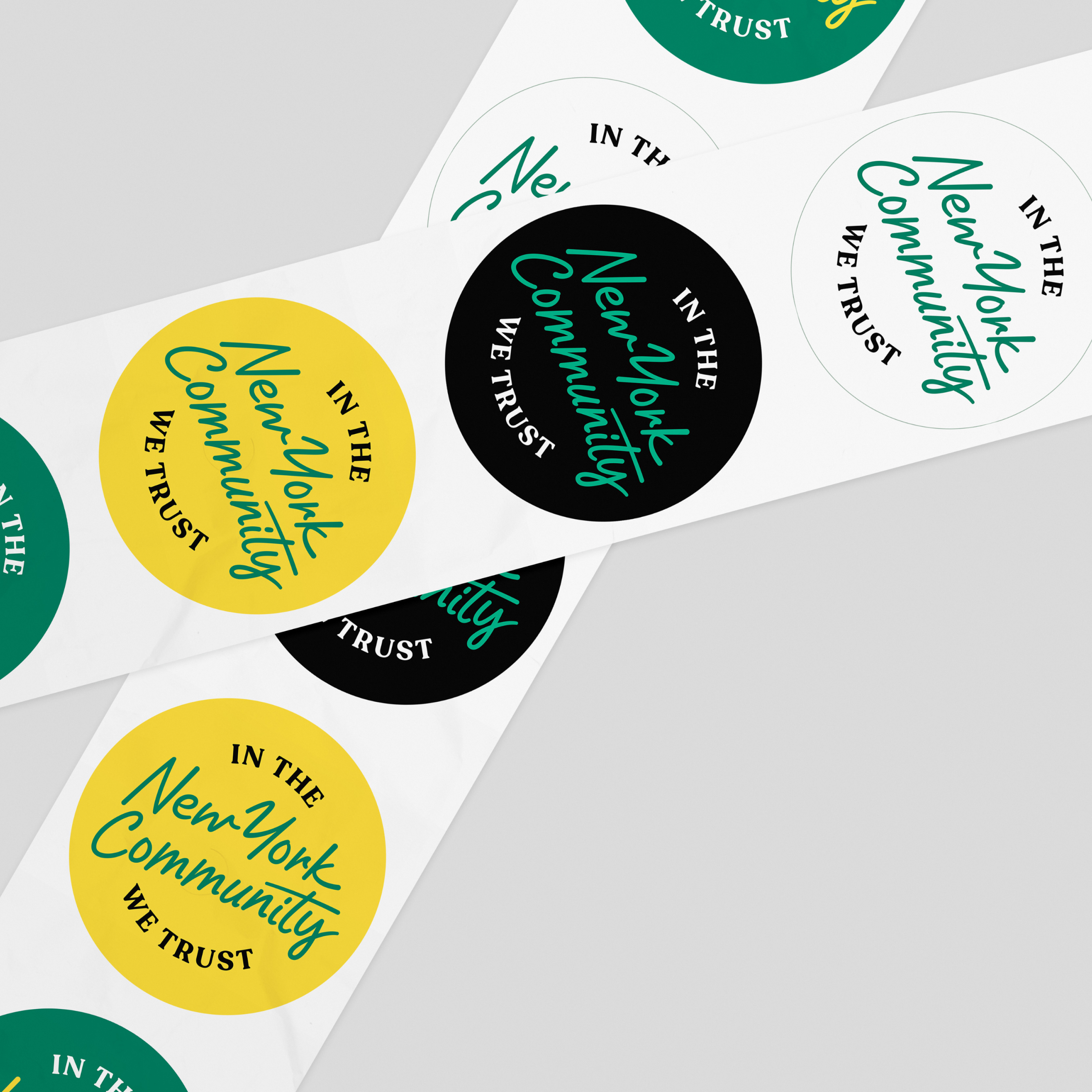 A set of round stickers with the phrases "In the New York Community We Trust" in various colors and fonts. The stickers feature black, white, yellow, and shades of green backgrounds and are arranged in a crisscross pattern on a light gray surface.