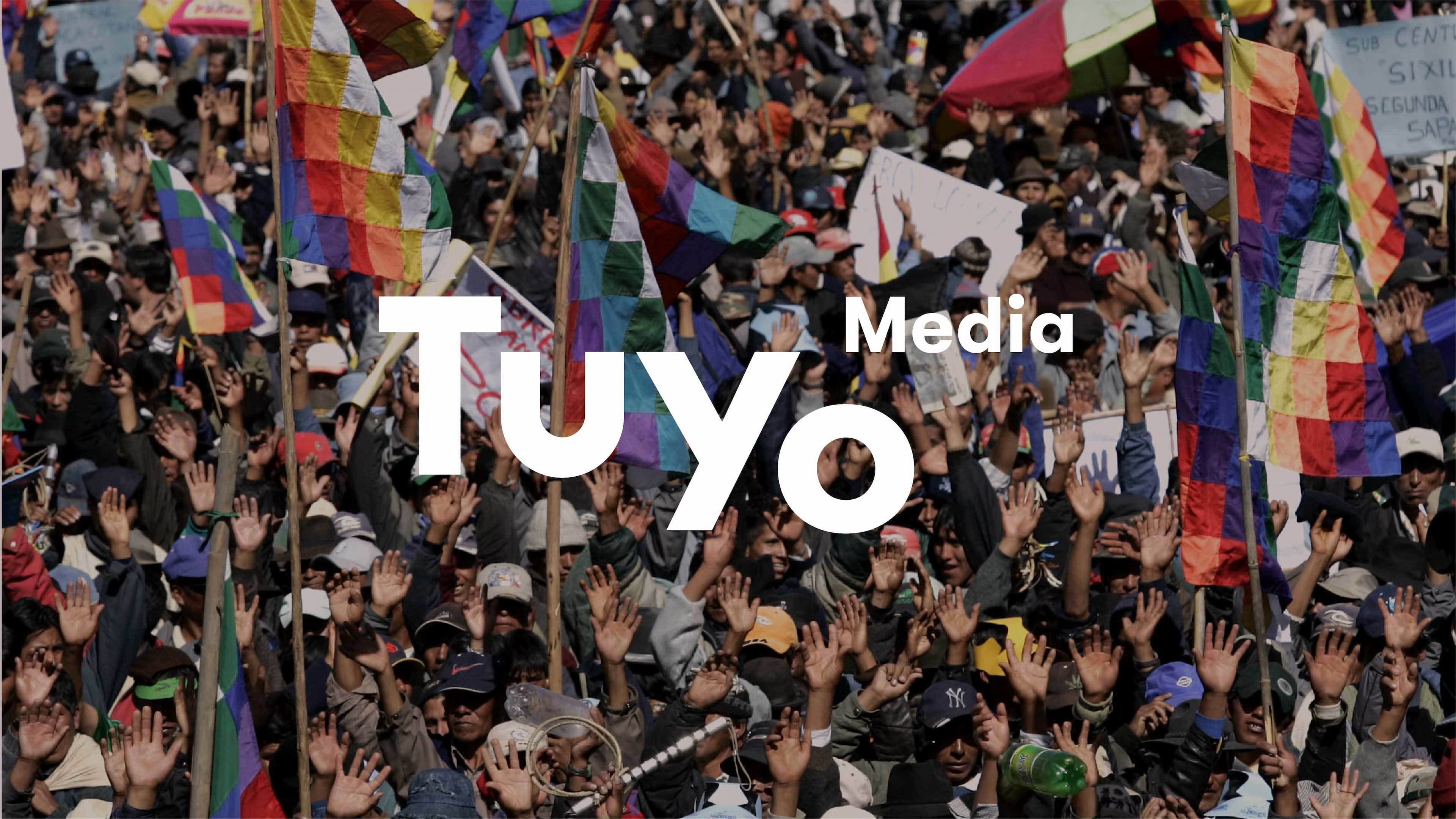 A large crowd of people, many waving colorful flags, is shown in a lively protest. The text "Tuyo Media" is prominently displayed over the image. The vibrant flags and raised hands create a dynamic and energetic atmosphere.