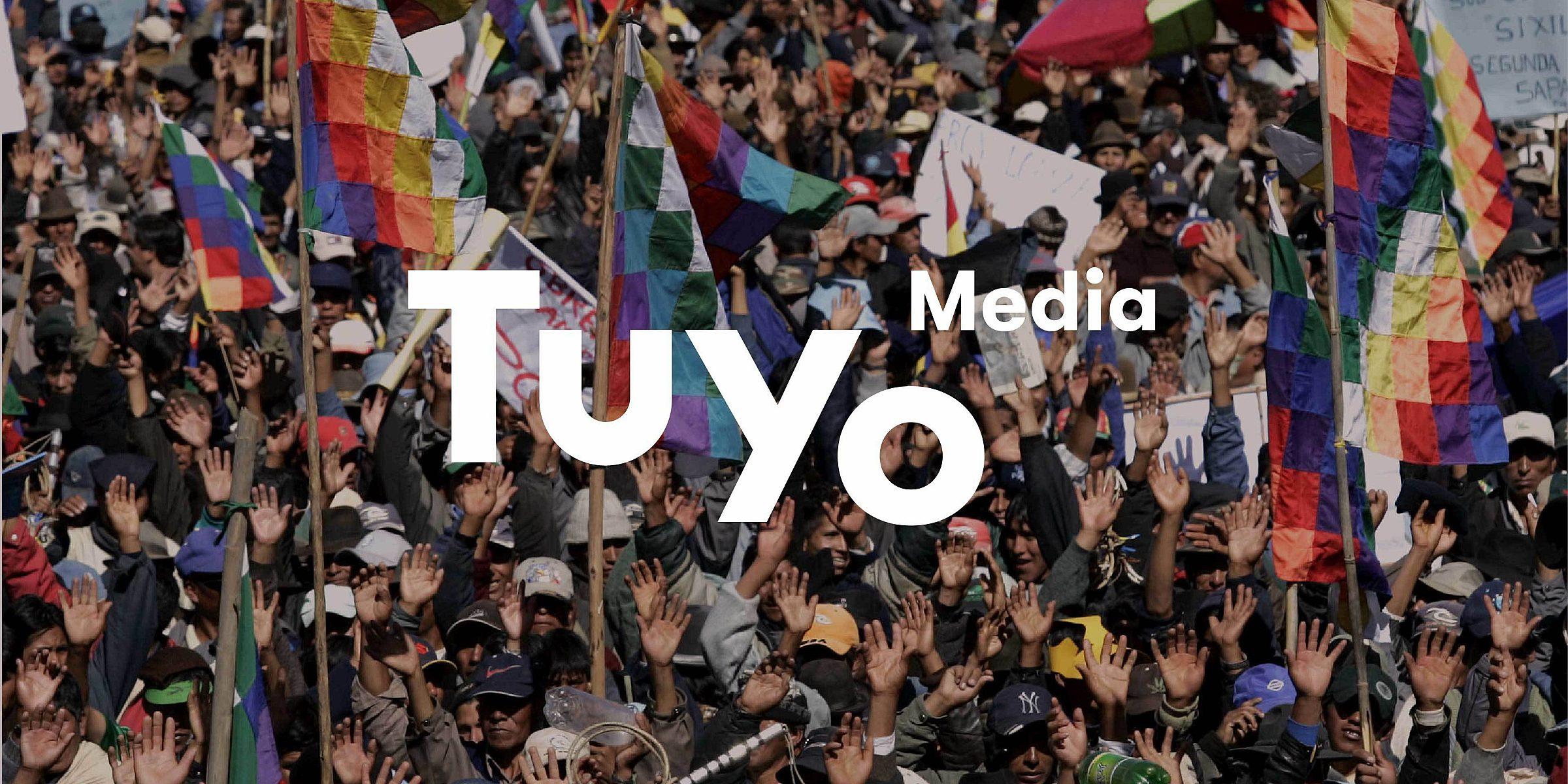 A large crowd of people, many waving colorful flags, is shown in a lively protest. The text "Tuyo Media" is prominently displayed over the image. The vibrant flags and raised hands create a dynamic and energetic atmosphere.