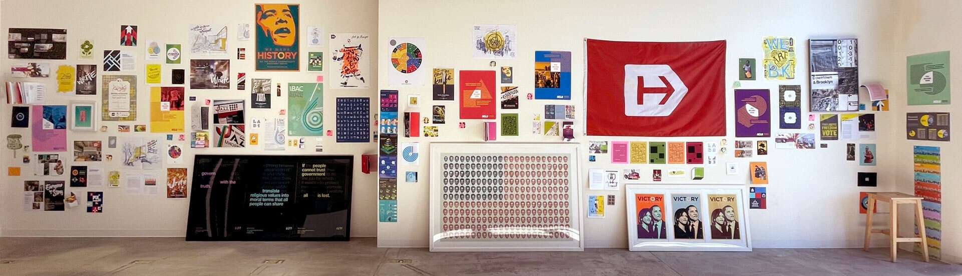 A large wall is covered with various posters, artwork, and images, creating an eclectic collage. There's a prominent red flag with a white emblem on the right side, and numerous colorful graphics and photos spread across the entire wall.