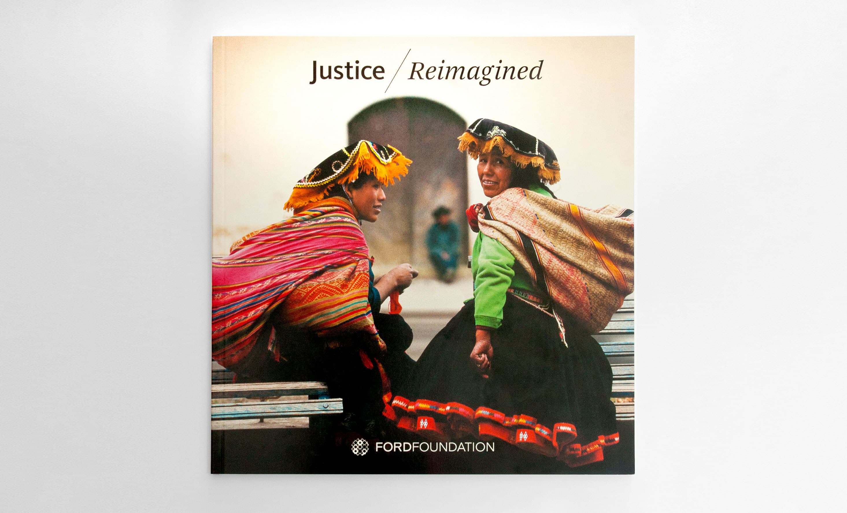 The cover of a book titled "Justice Reimagined" published by the Ford Foundation. It features a photograph of two people dressed in traditional Andean clothing, sitting and engaging with each other, against a blurred outdoor background.