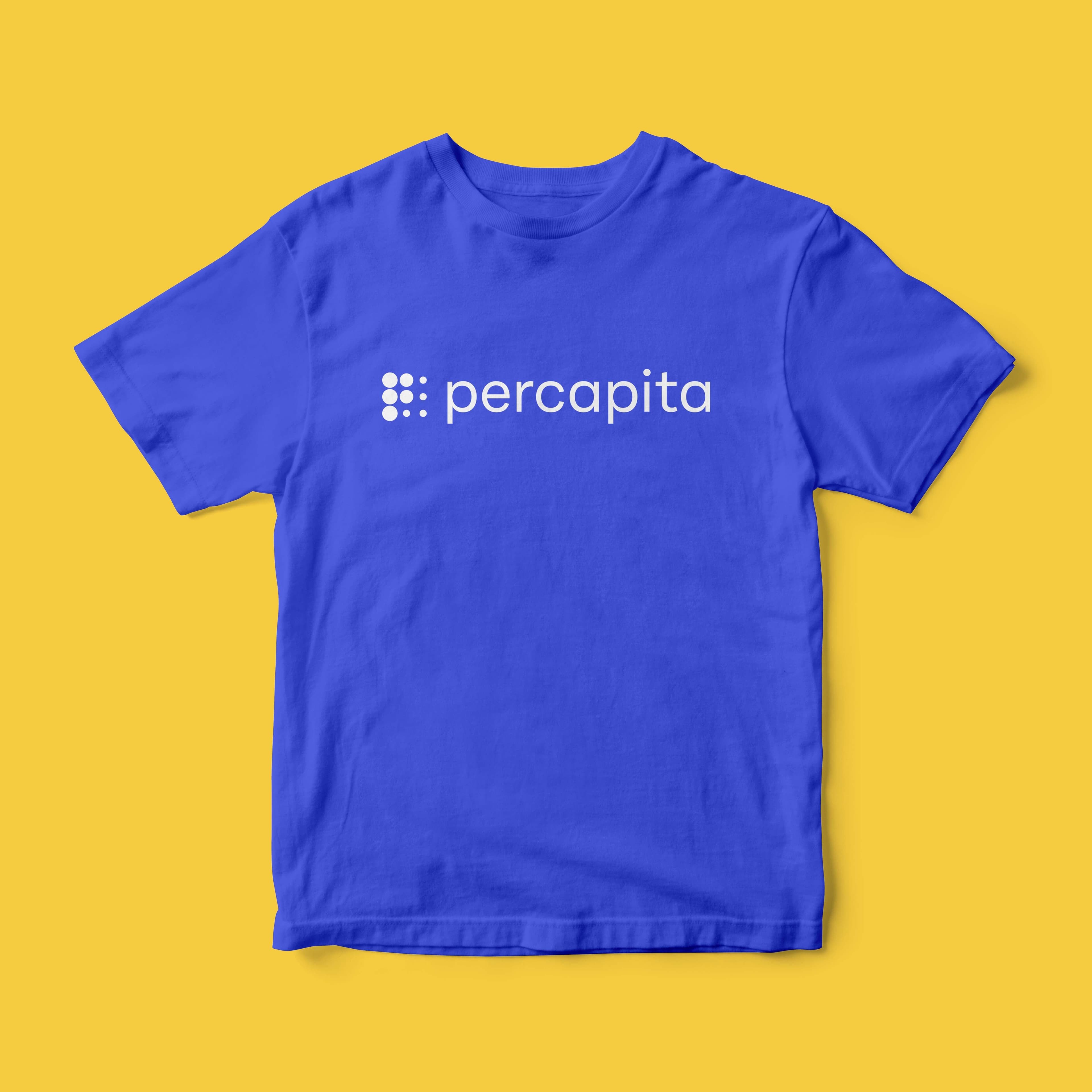 A royal blue T-shirt on a yellow background features the word "percapita" in white lowercase letters centered on the chest. Above the text, there is a logo consisting of nine dots arranged in a 3x3 grid, also in white.