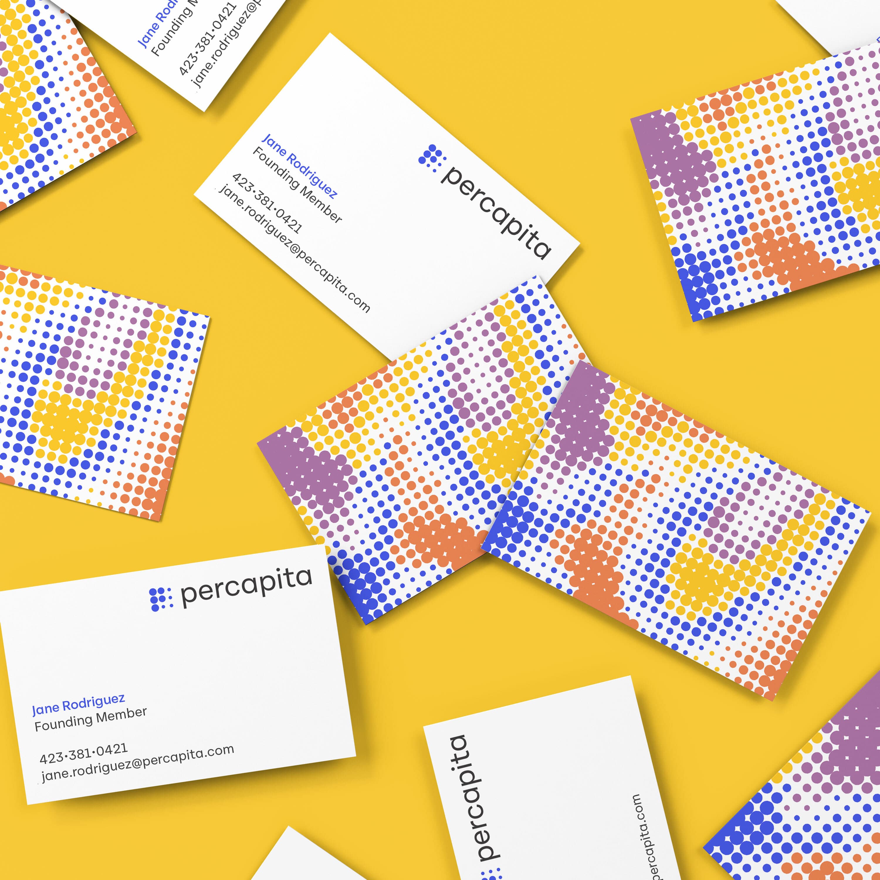 Scattered business cards on a yellow background. The cards feature a colorful dot pattern in purple, yellow, and red on one side, and text details on the other. Key information includes a name, position, phone number, and email address, alongside a logo with "percapita.