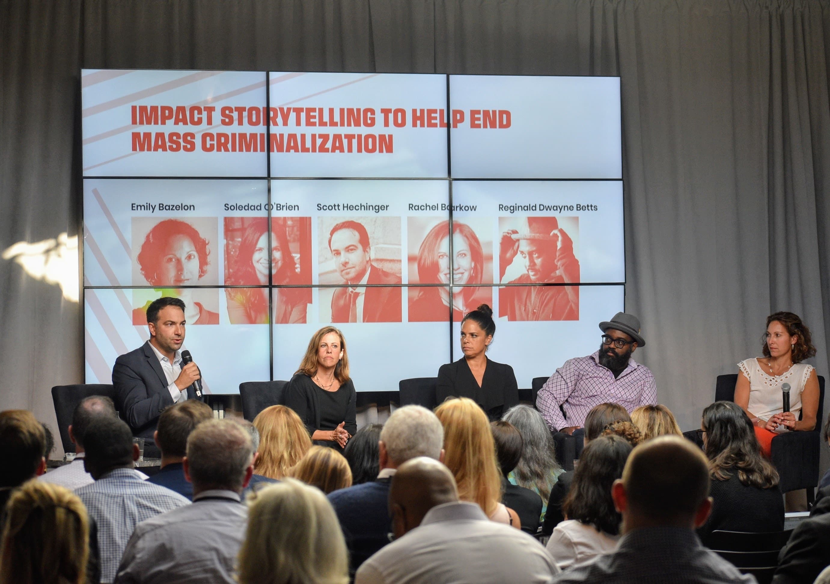 A panel of five speakers sits on stage in front of a large audience. Behind them, a screen displays their names: Emily Bazelon, Soledad O’Brien, Scott Hechinger, Rachael Rollins, and Reginald Dwayne Betts, under the title "Impact Storytelling to Help End Mass Criminalization.